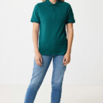 Femme portant un polo vert et jean bleu.