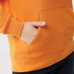 Main dans la poche d’un sweat orange
